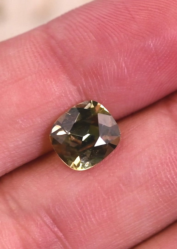 Video of natural yellow green Tanzanite cushion brilliant cut rotating under light, demonstrating sparkle, facet reflections, and untreated color from Merelani Hills, Tanzania