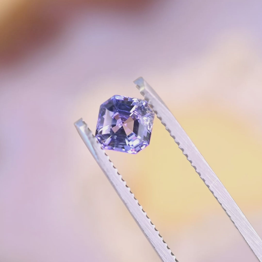 1.14 carat untreated pink purple blue Tanzanite Asscher cut rotating in tweezers under natural light, Merelani Hills Tanzania gemstone showing step cut brilliance and color shift for custom jewelry