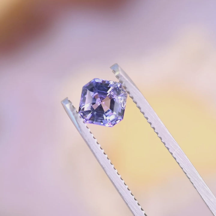 1.14 carat untreated pink purple blue Tanzanite Asscher cut rotating in tweezers under natural light, Merelani Hills Tanzania gemstone showing step cut brilliance and color shift for custom jewelry