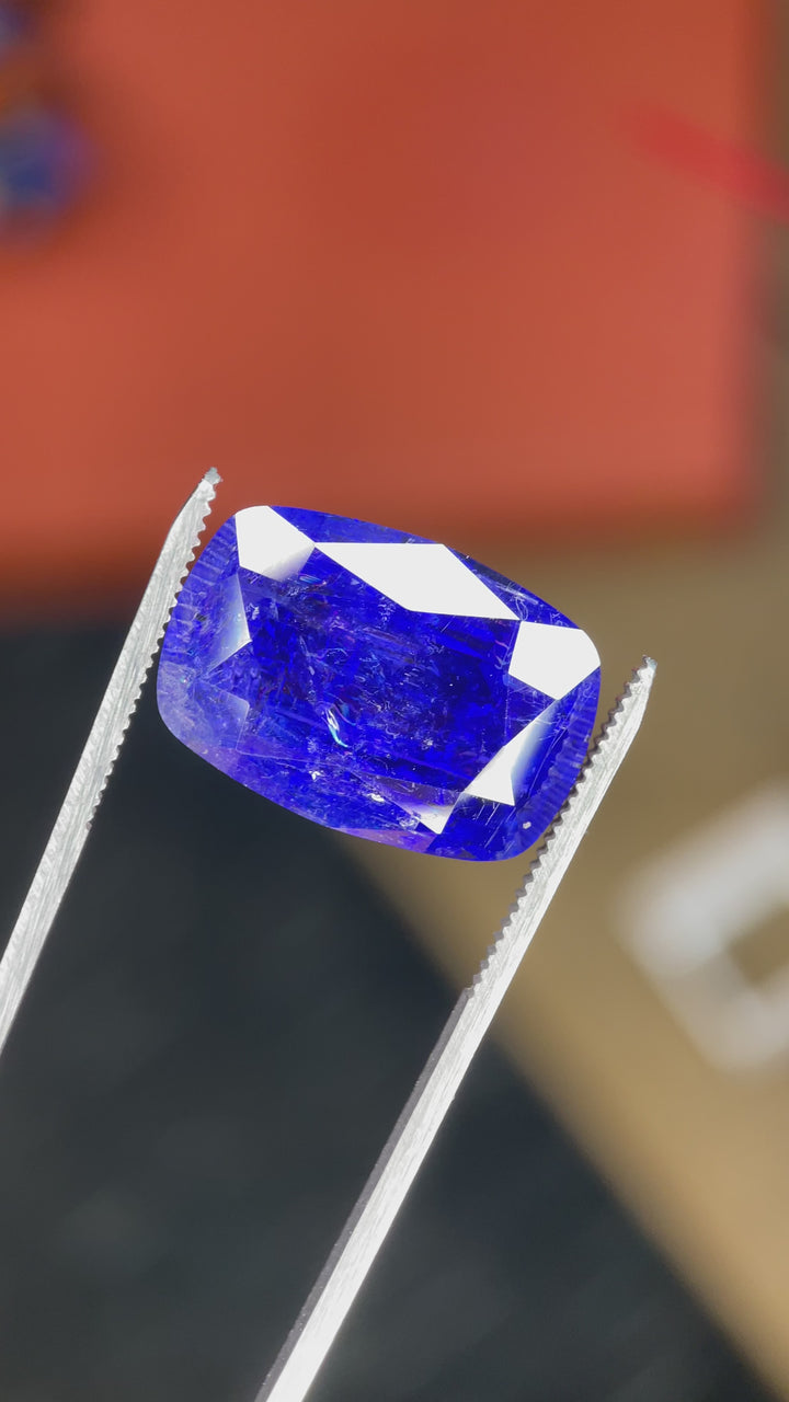 A rotating video of a 27.31-carat cushion-cut tanzanite, displaying its vivid royal blue and purple hues and internal clarity under bright lighting.