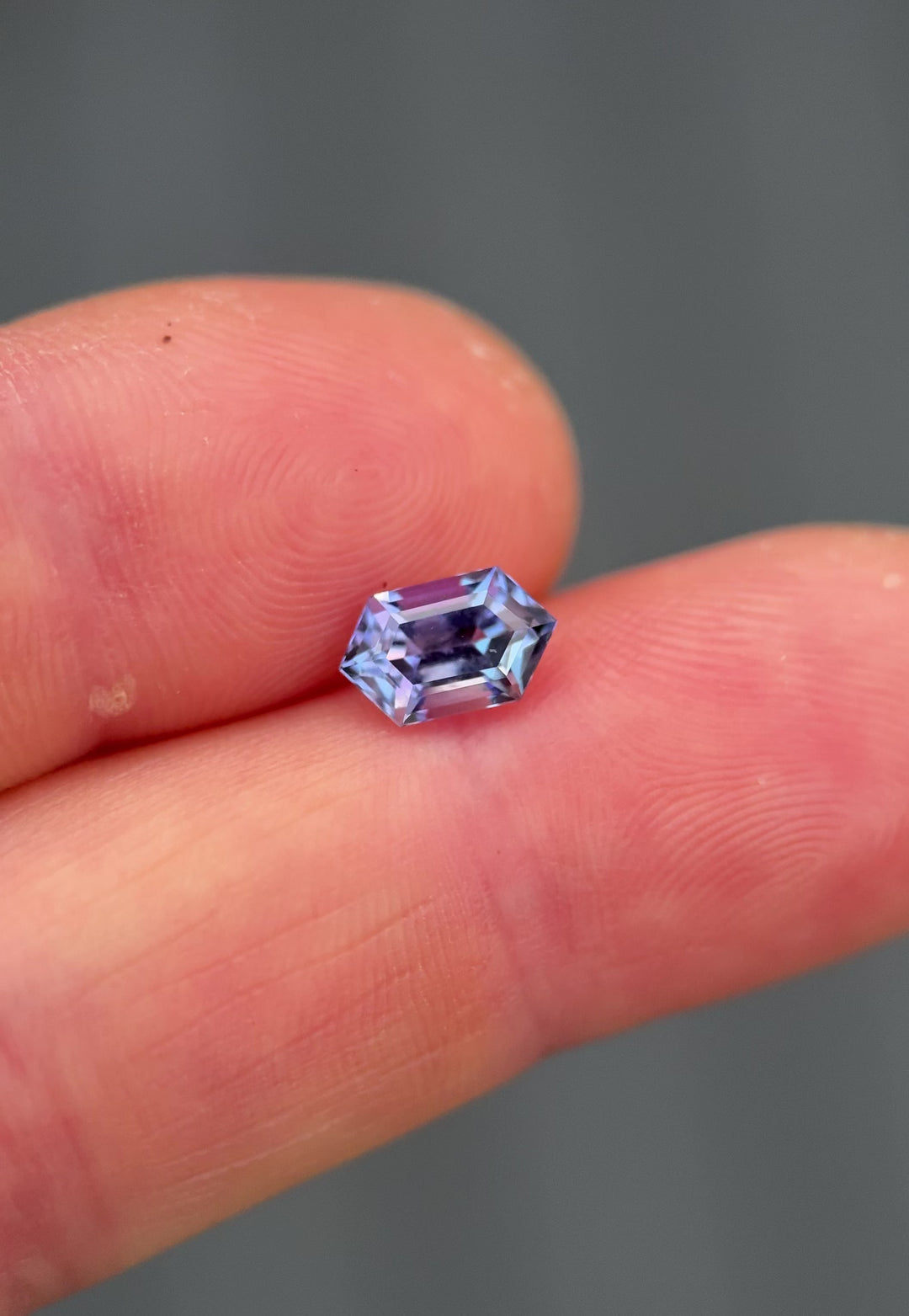 Handheld video of a 1.43-carat untreated tanzanite in a step cut hexagon, moved to show color play between blue, green, pink, and purple mermaid tones, capturing brilliance and faceting from various angles.