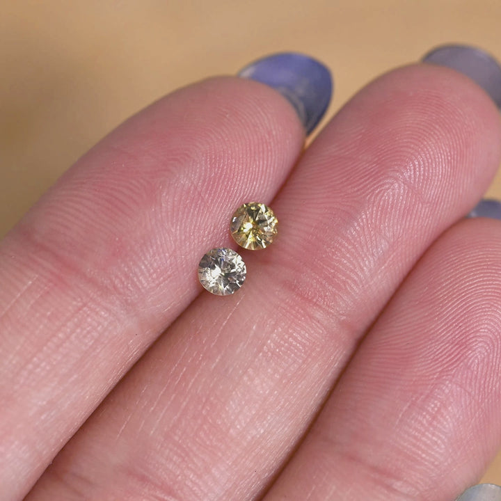 Rotating loose matching pair of yellow, teal and green Montana sapphires shown on hand, revealing the brilliance and shifting color of the round brilliant cut.