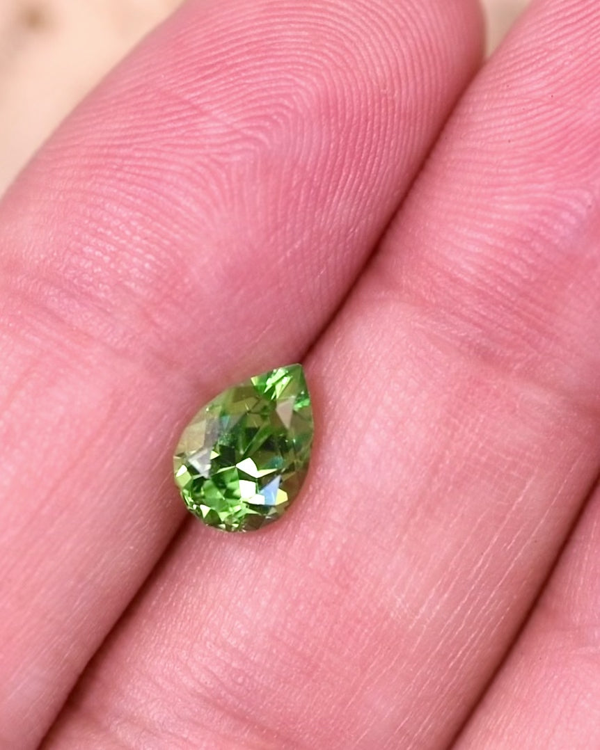 Close-up video of 1.39 carat tsavorite garnet resting on fingertips, showing dynamic sparkle and depth of color as light reflects off the pear cut facets, natural unheated gemstone from Kenya.
