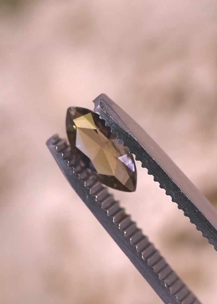 Close-up video of a marquise brilliant cut tanzanite being examined in tweezers, showing yellow, teal, and green hues, facet precision, and untreated clarity from Tanzania