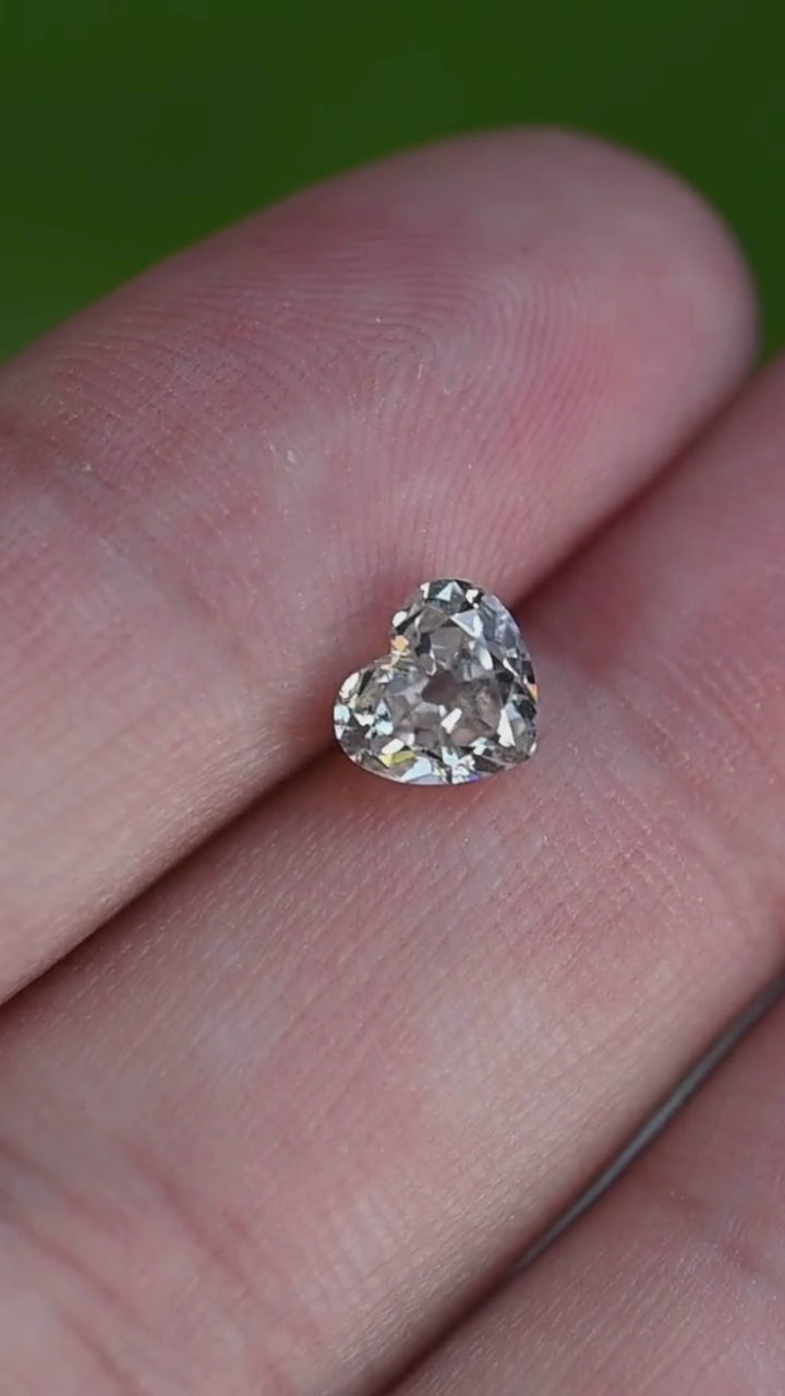 Video of a natural 1.21 carat antique style heart cut salt and pepper diamond held in gem tweezers, rotating to reveal vintage faceting, white sparkle, and distinctive internal inclusions.