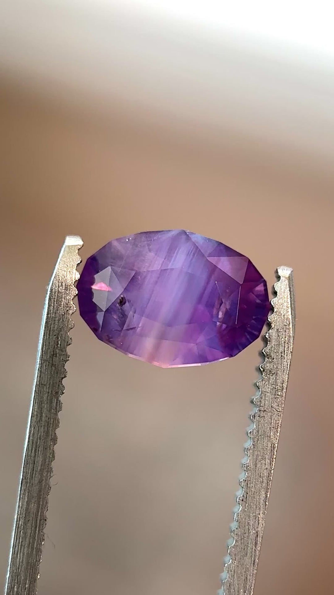 Natural unheated purplish pink sapphire held in tweezers, highlighting brilliant oval symmetry and soft lavender-pink glow.