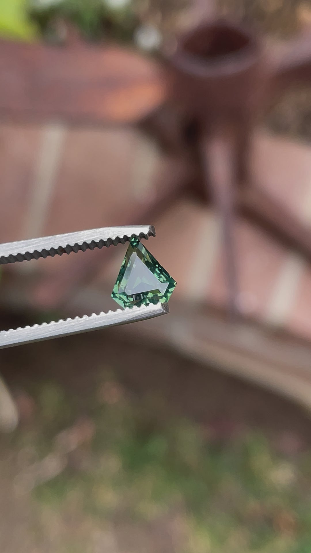 Video showcasing a 1.57ct shield-cut sapphire in natural light, revealing opalescent shades of yellow, teal, and green with a step-cut precision from different angles.