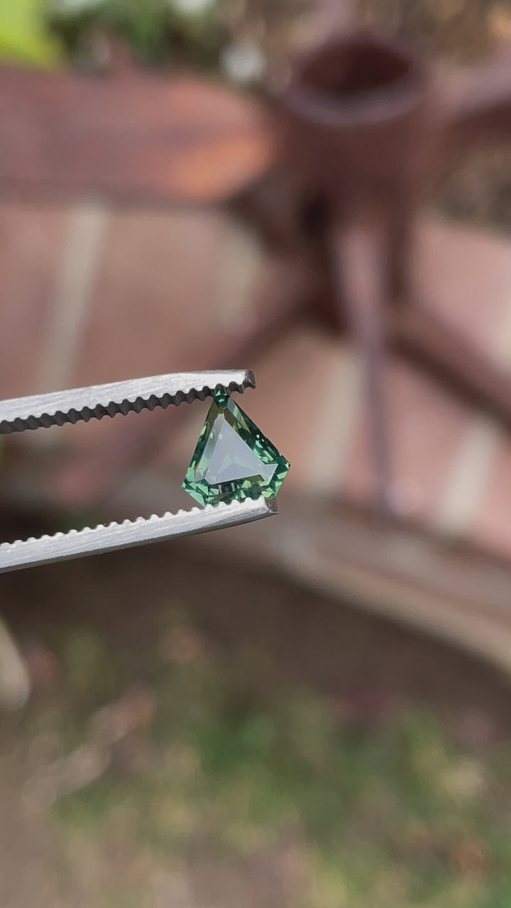 Video showcasing a 1.57ct shield-cut sapphire in natural light, revealing opalescent shades of yellow, teal, and green with a step-cut precision from different angles.