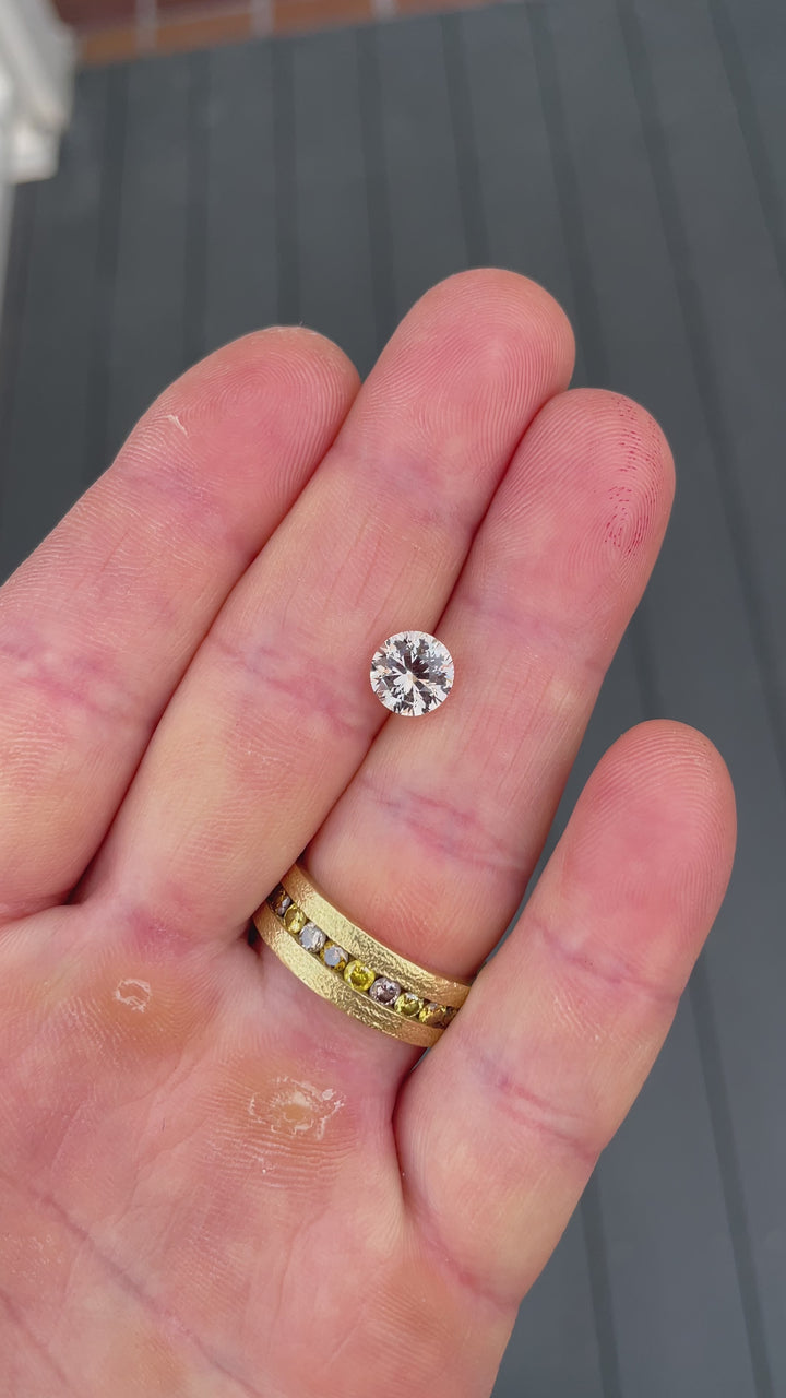 A detailed video capturing the light performance and elegance of a 2.57-carat peach sapphire in round brilliant cut, filmed with dynamic lighting.