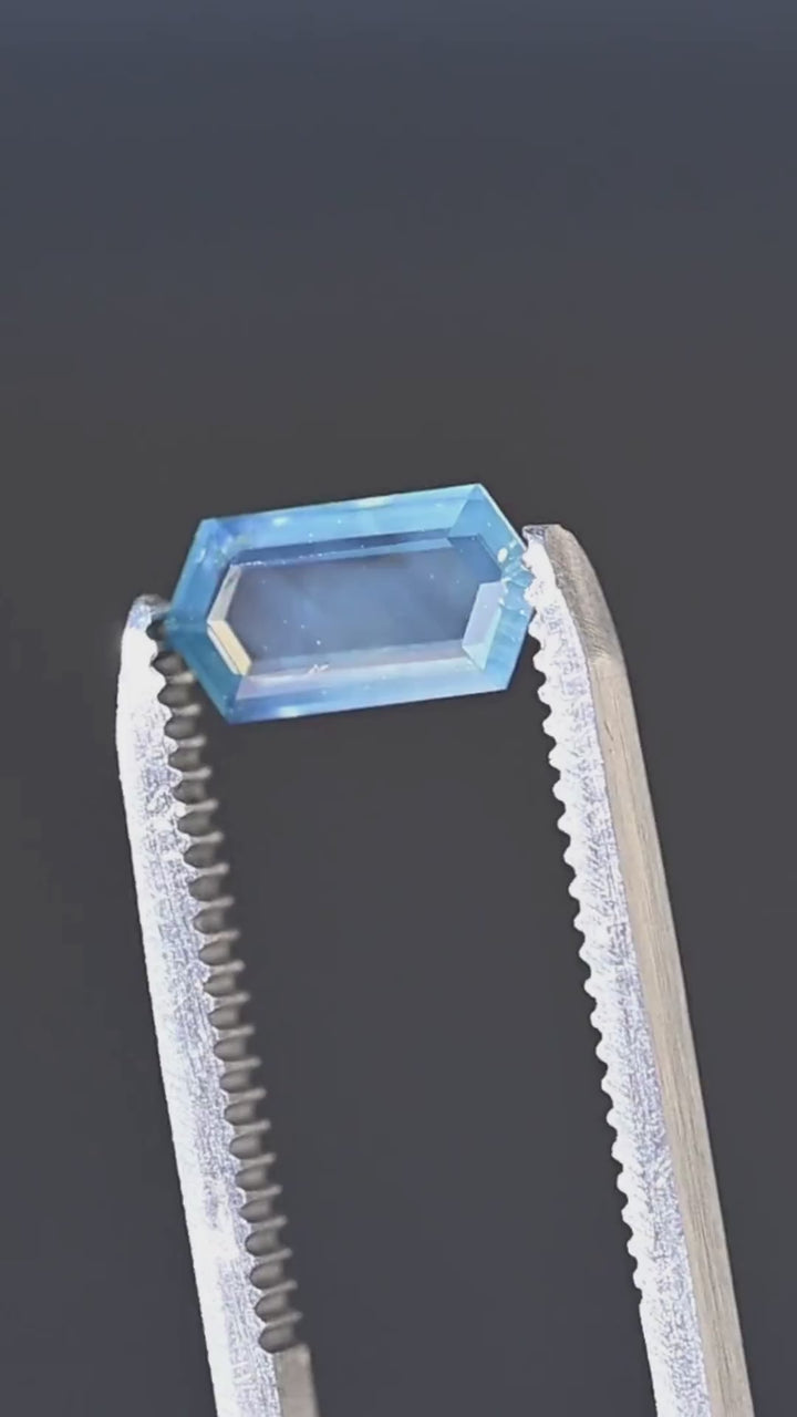 Explore the geometric character of this untreated 1.55ct opalescent teal blue sapphire from Nigeria. Presented in jeweler's tweezers, its elongated hexagonal portrait cut features a broad central window, crisp step facets and a distinctive contrast between soft seafoam blue and saturated teal.