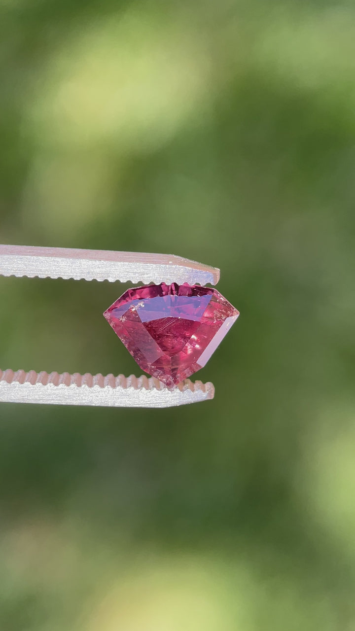 Rotating video of a 2.94-carat shield step-cut sapphire from Umba River, Tanzania, displaying vivid flashes of strawberry red and dusty rose mauve under shifting natural light.