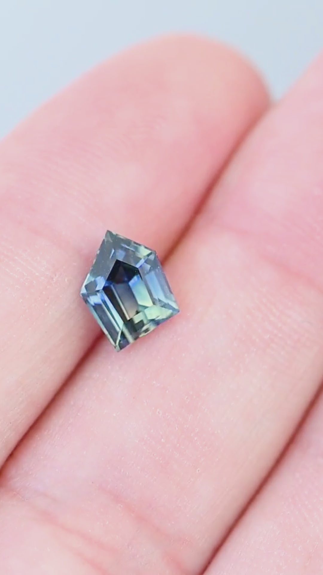 Untreated 1.70 carat Madagascar parti sapphire moving on a hand, revealing changing blue, teal, green and yellow color zones across its asymmetrical geometric step facets.