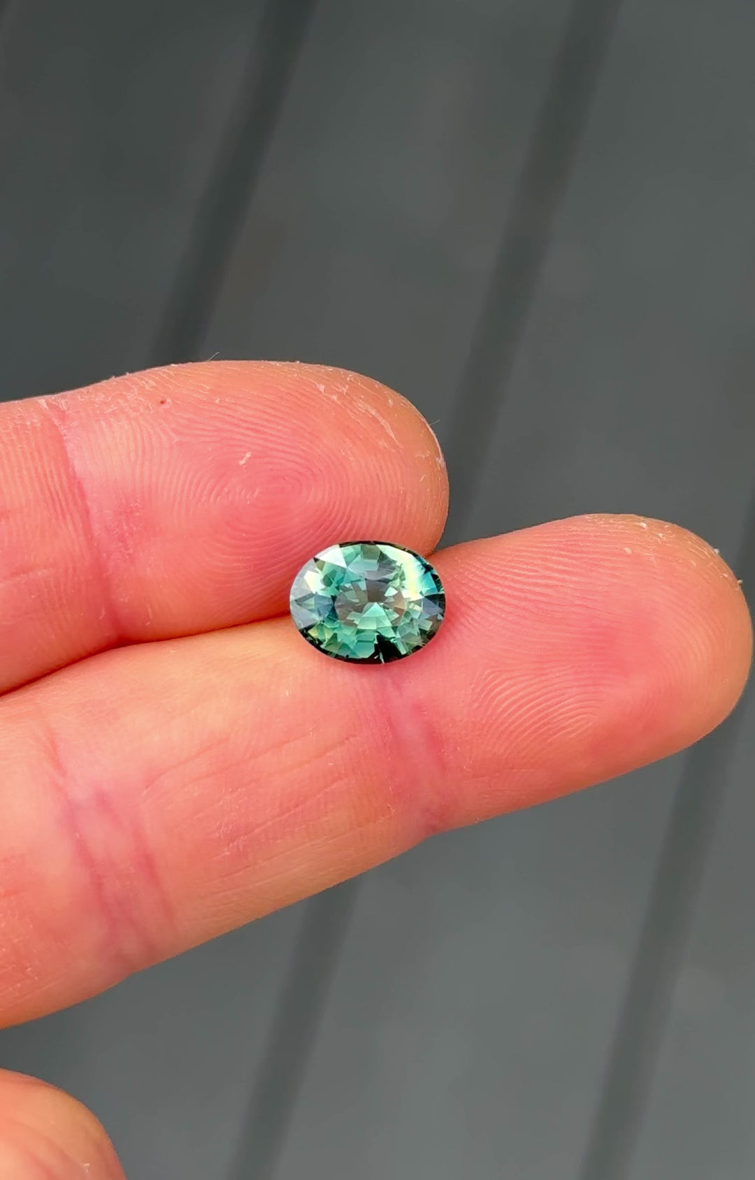 Handheld video of 3.02CT oval parti sapphire from Madagascar, highlighting shifting yellow, teal, blue, and green tones as the gem moves in the light.