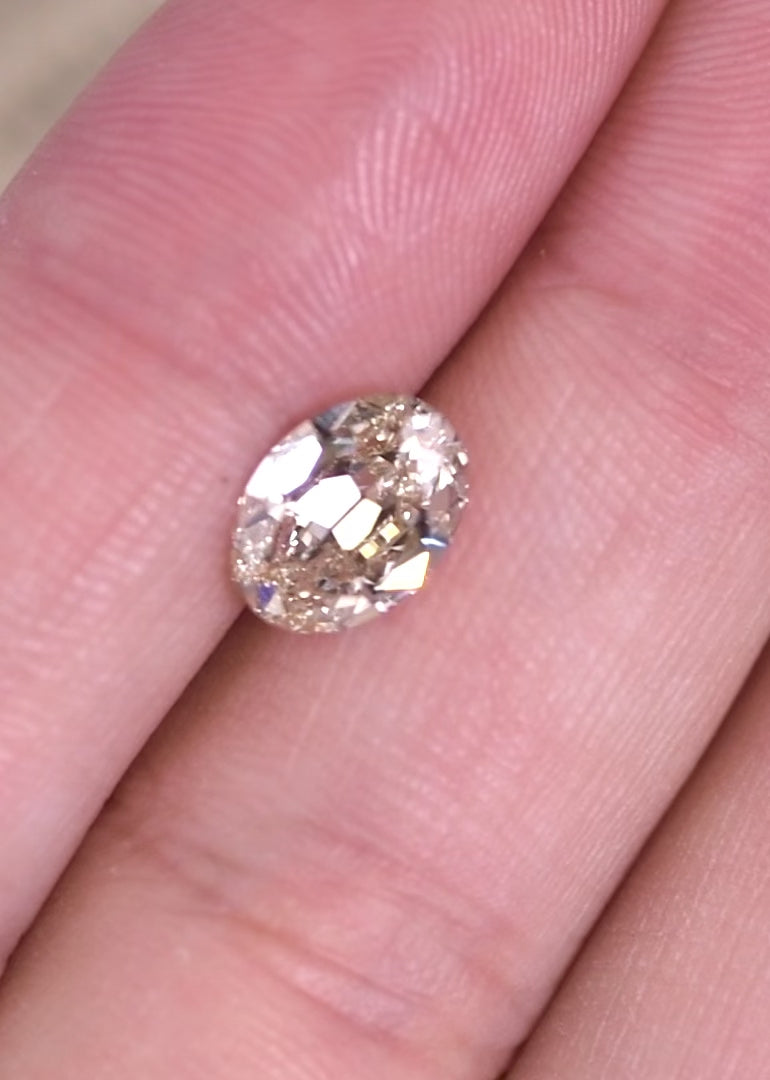 Rotating oval diamond with light rosy brown color showing brilliance and facet movement in natural lighting.