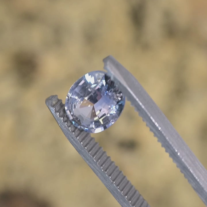 Video of a 2.25ct gray clear pink oval sapphire rotating in tweezers, untreated Sri Lankan sapphire showing light performance and mix cut faceting