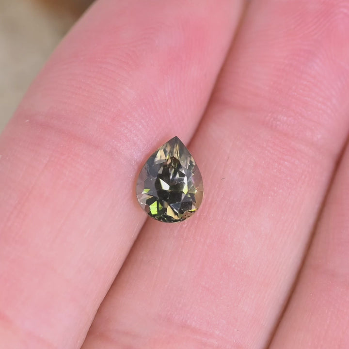 Close up video of 1.32ct pear cut Tanzanite displaying brilliant faceting sparkle and trichroic green brown purple tones for fine jewelry