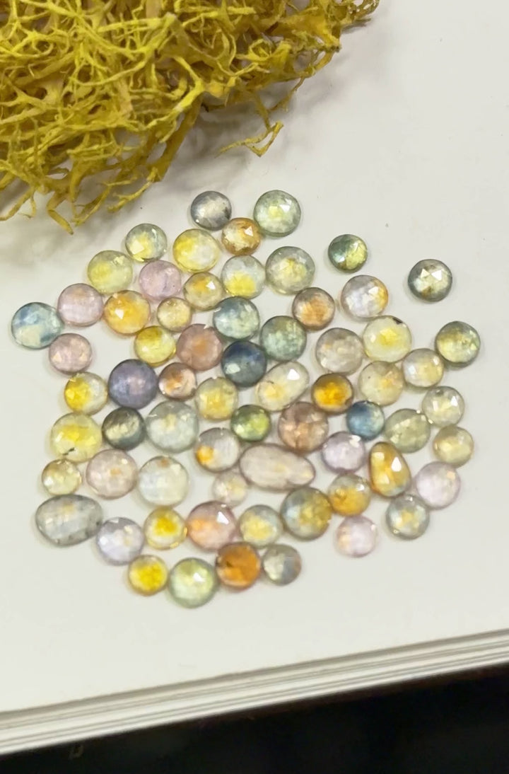 Close-up video of fancy parti Montana sapphires in teal blue, green, yellow, orange, purple, and pink shades from the Eldorado Deposit, gently moved under light to highlight brilliance and color play. Heated gemstones in mixed round, oval, and freeform cuts totaling 17.40 carats.