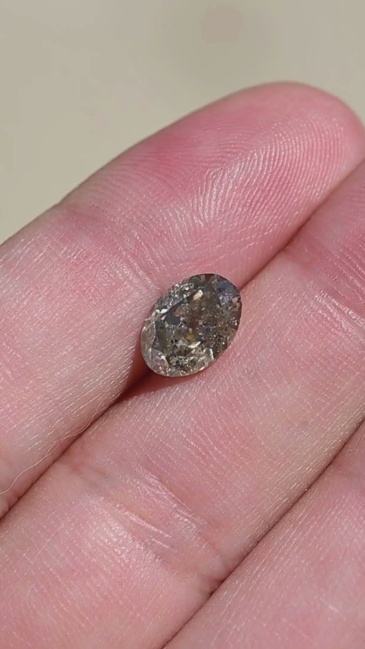 1.88 carat fancy greenish brown grey salt and pepper diamond rotating in hand, showing its elongated antique oval brilliant cut, earthy coloration and visible natural inclusions.