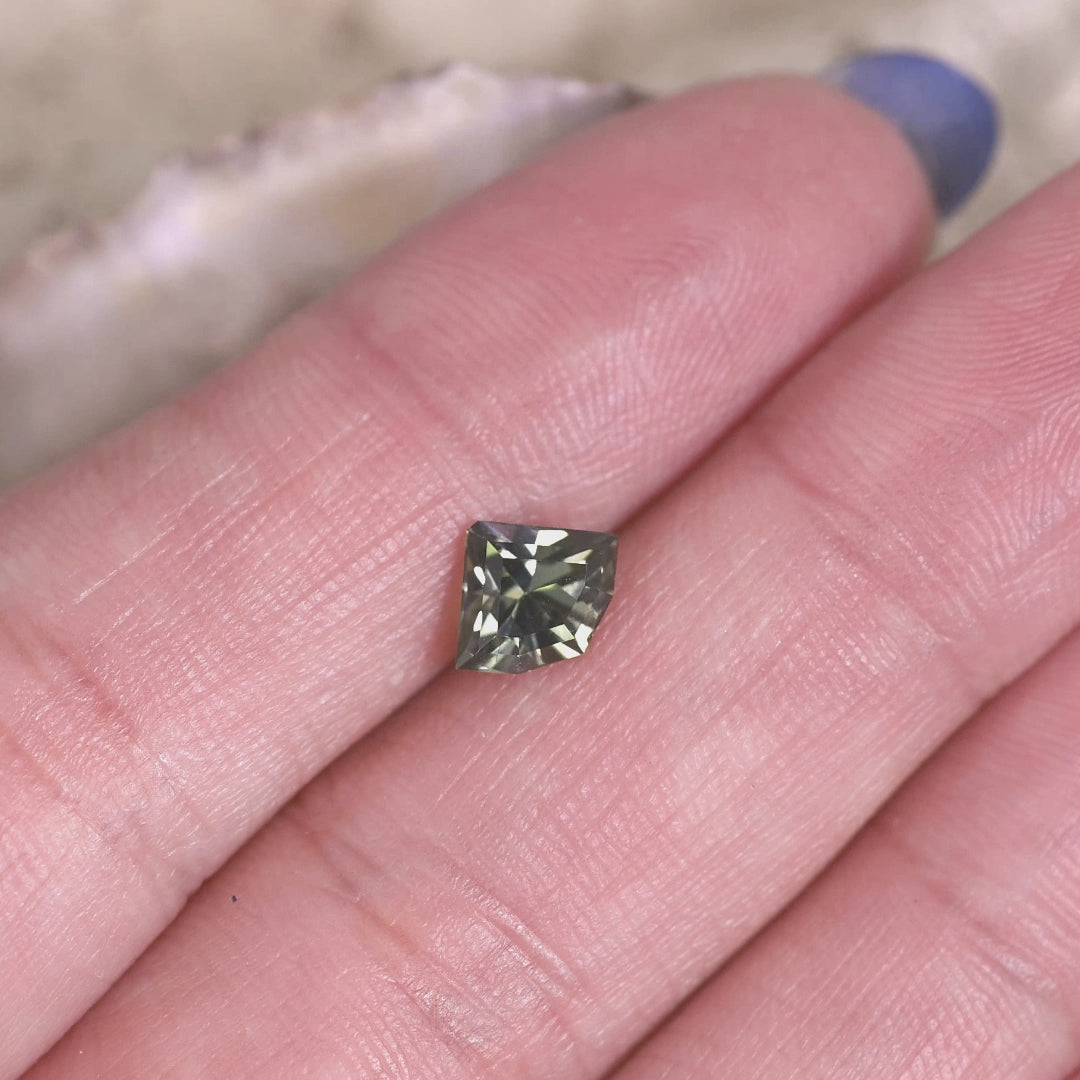 Loose teal and green tanzanite rotating on hand, showing the custom shield mix cut and subtle shifts between green and yellow tones in natural light.