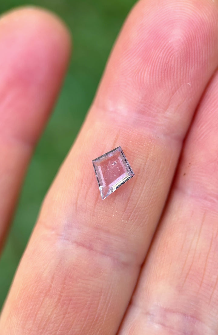 Untreated Colombian kite-cut sapphire rotating in tweezers under daylight, showcasing soft pink-lavender hues and refined portrait-style step cut.