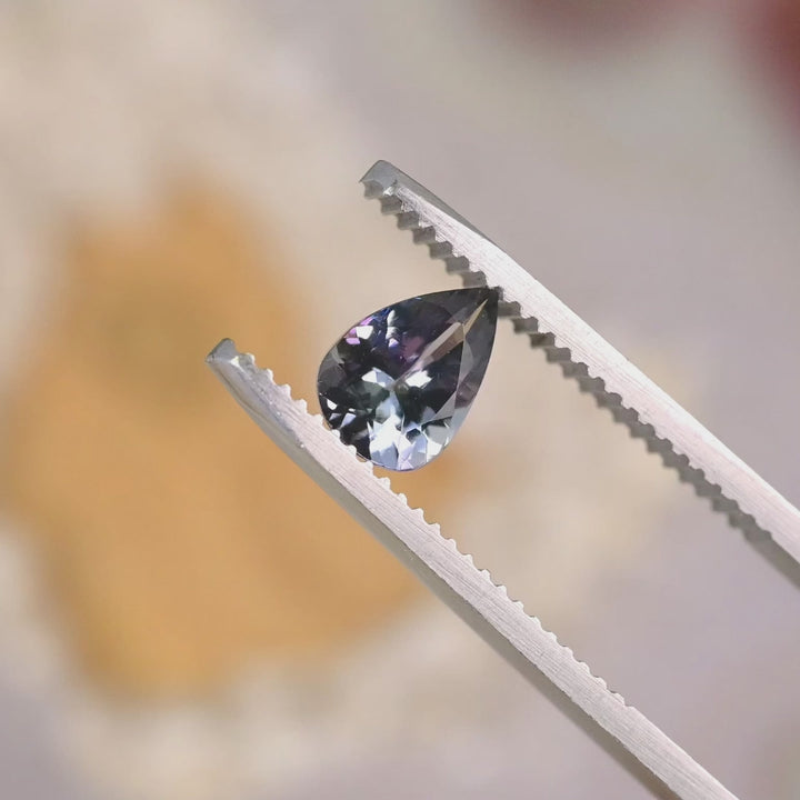 1.10 carat violet teal pear cut Tanzanite rotating on hand under natural light, modified brilliant gemstone from Merelani Hills showing vivid color shift and sparkling custom jewelry brilliance