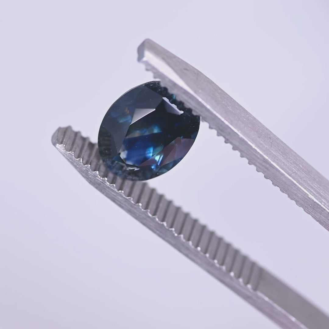 Heated 2.62 carat Montana blue sapphire oval mix cut turning in tweezers, highlighting sparkle, depth and rich navy tone from El Dorado Bar