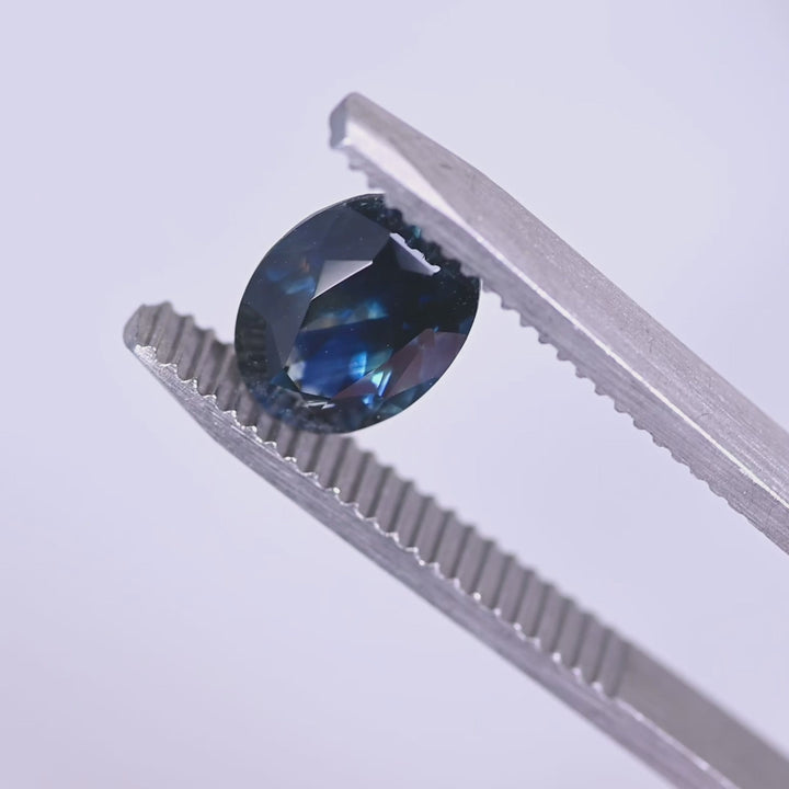 Heated 2.62 carat Montana blue sapphire oval mix cut turning in tweezers, highlighting sparkle, depth and rich navy tone from El Dorado Bar