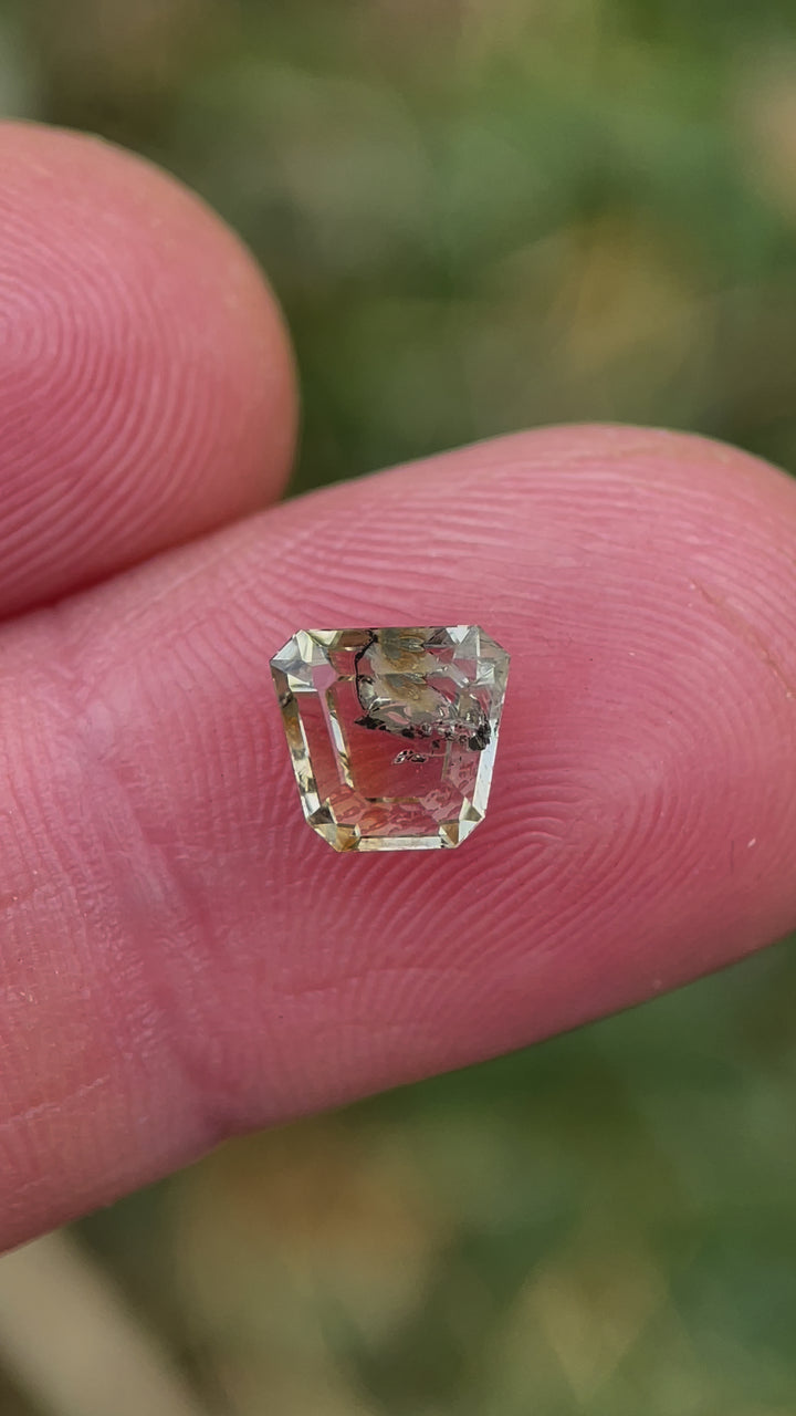 A vibrant 1.68-carat earthy yellow-green sapphire held in fingertips, reflecting natural sunlight as it is rotated to display its cut and color play.