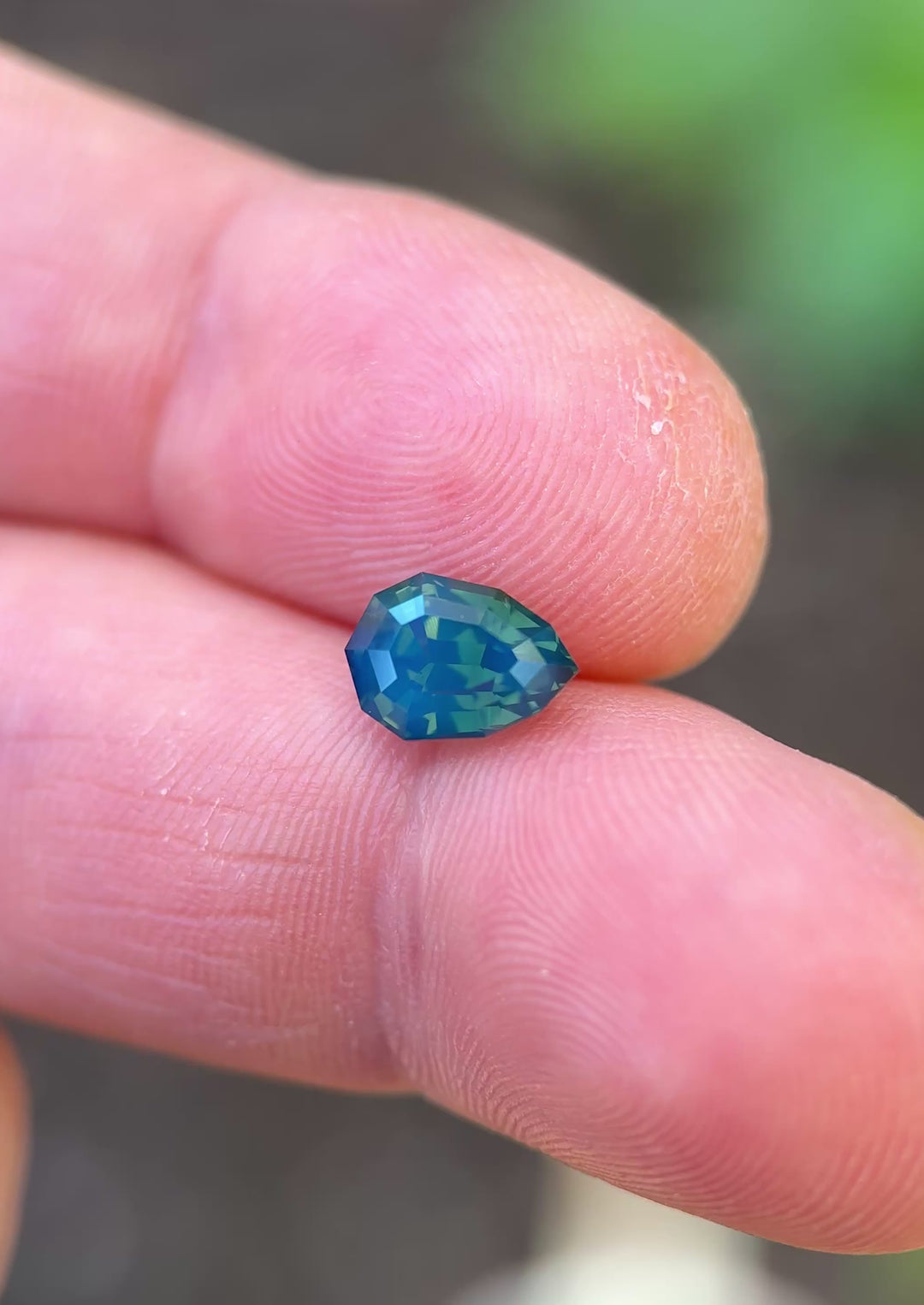 2.51ct opalescent teal blue green sapphire rotating in hand, revealing shifting ocean-inspired colors and crisp shield step-cut geometry.