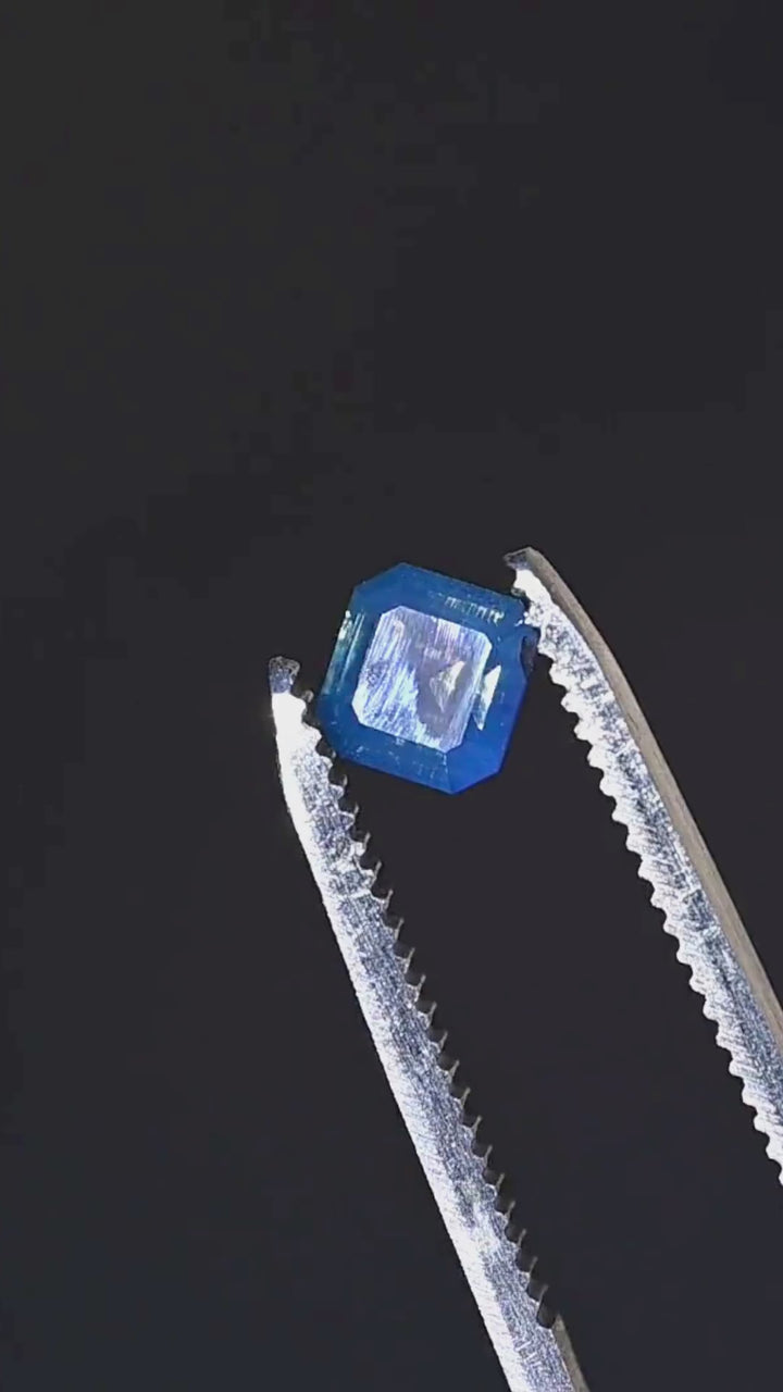 A close-up presentation of a natural 1.08ct opalescent denim blue sapphire from Gombe, Nigeria. Its squared octagonal step cut features broad facets, clipped corners and saturated blue coloration.