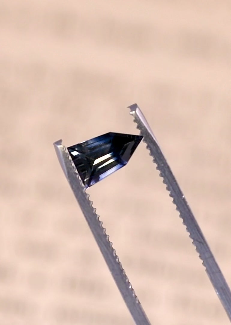 Rotating video of a bi-color parti sapphire held in tweezers, revealing colorless to blue color zoning and step cut pentagon shield geometry, 1.22ct untreated sapphire from Sri Lanka