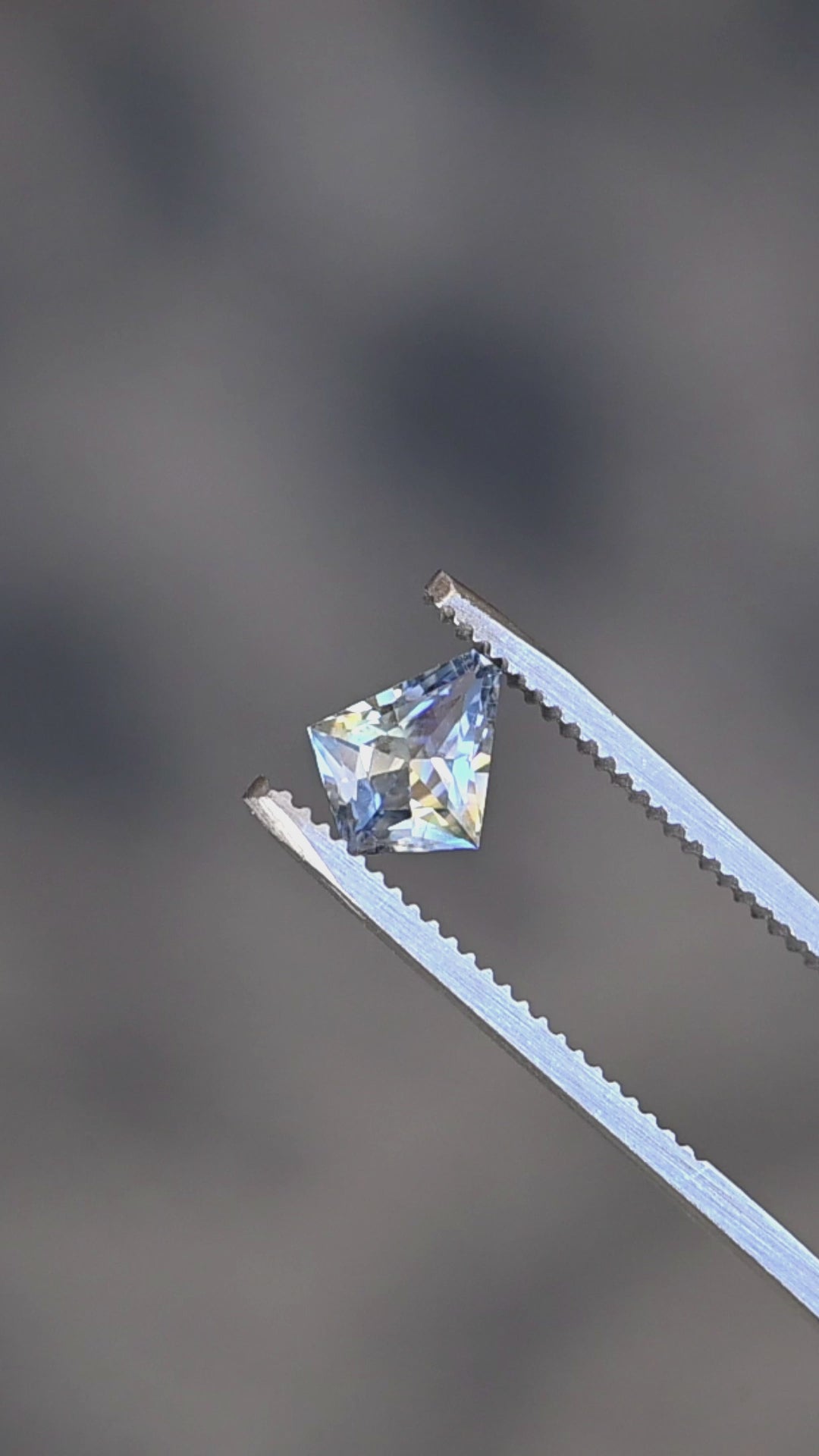1.20ct Blue Yellow Parti custom kite cut sapphire rotating in gem tweezers under natural light.