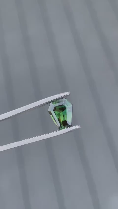 Video showcasing the exceptional clarity and vibrant teal and green hues of a 2.38-carat sapphire from Madagascar. The gemstone, with its unique step cut coffin shape, is displayed in motion to highlight its natural beauty and the facets that enhance its brilliant color, illustrating its worth and no heat treatment.
