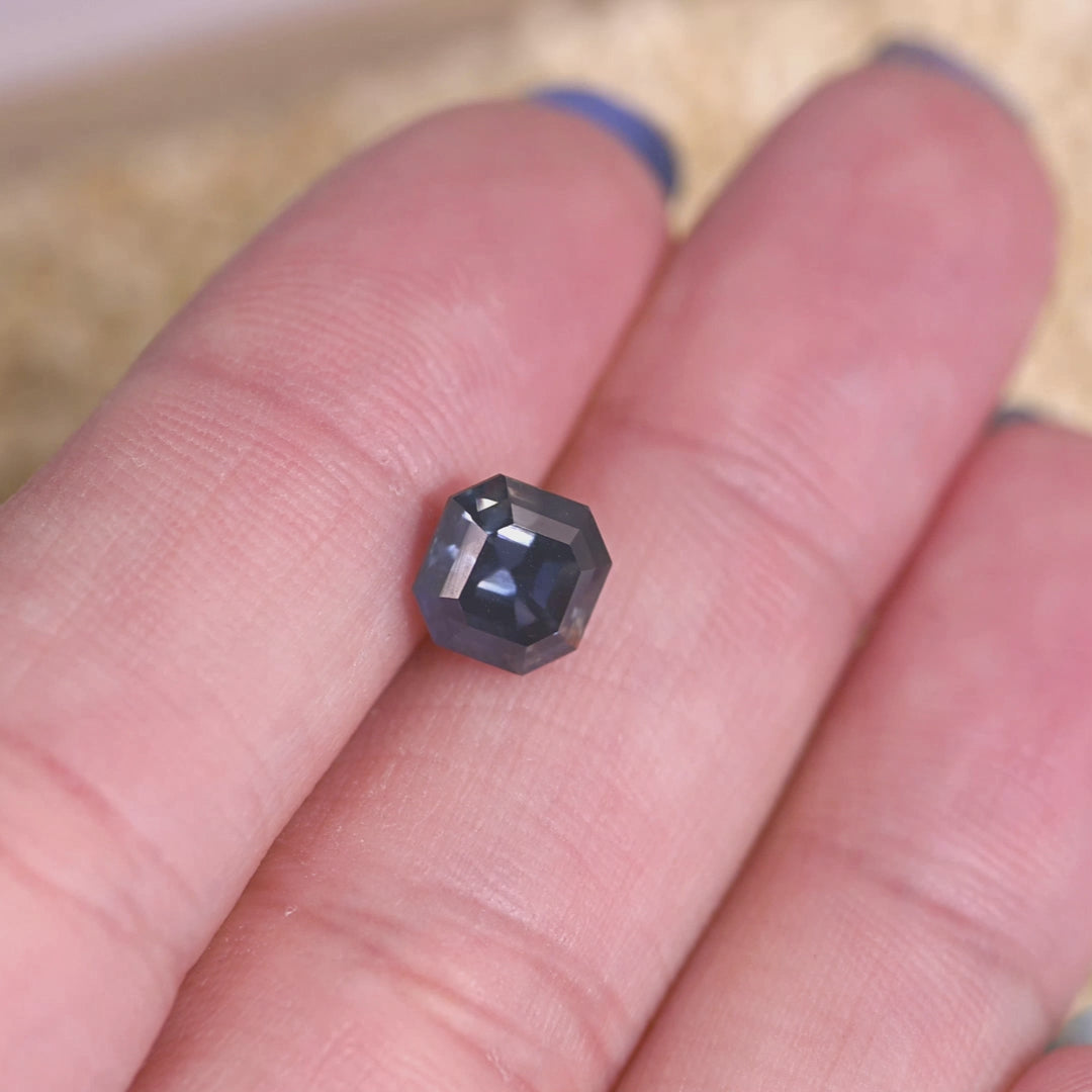 Loose precision Asscher cut sapphire turning in light, revealing natural color change from teal blue to grayish purple from Nigeria.