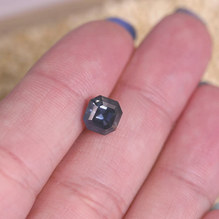 Loose precision Asscher cut sapphire turning in light, revealing natural color change from teal blue to grayish purple from Nigeria.