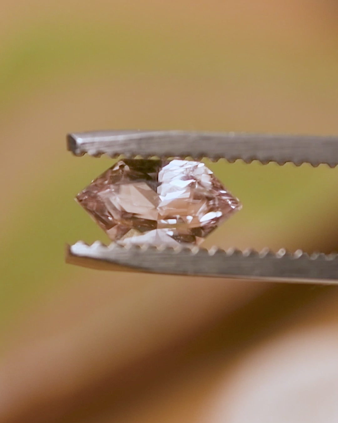 Rotation video of 1.17 carat champagne peach pink sapphire held in tweezers, revealing precision Dutch marquise hexagon cut facets and sparkling color play under natural light, untreated gem from Sakaraha, Madagascar.
