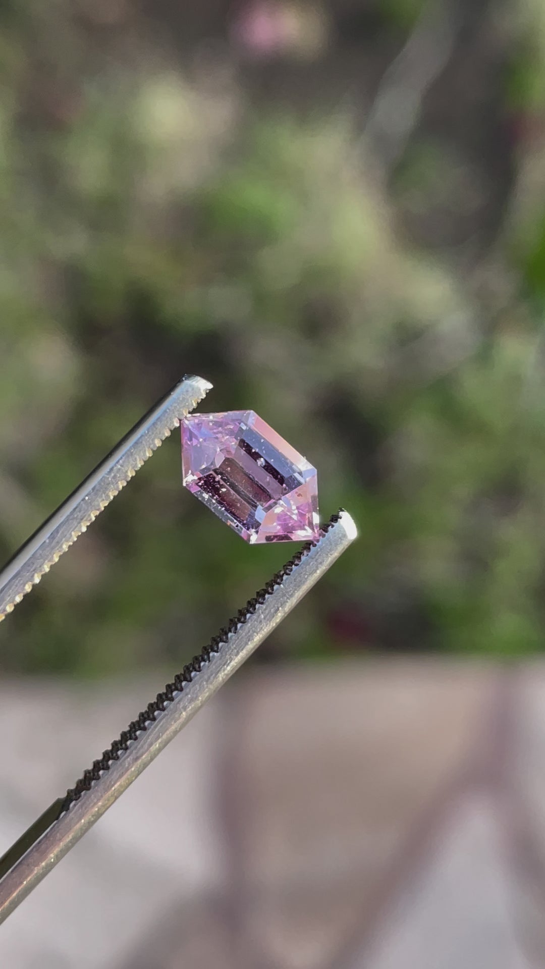 A step cut hexagon sapphire weighing 1.33 carats, displaying its pink, lavender, and champagne hues as it catches the light.
