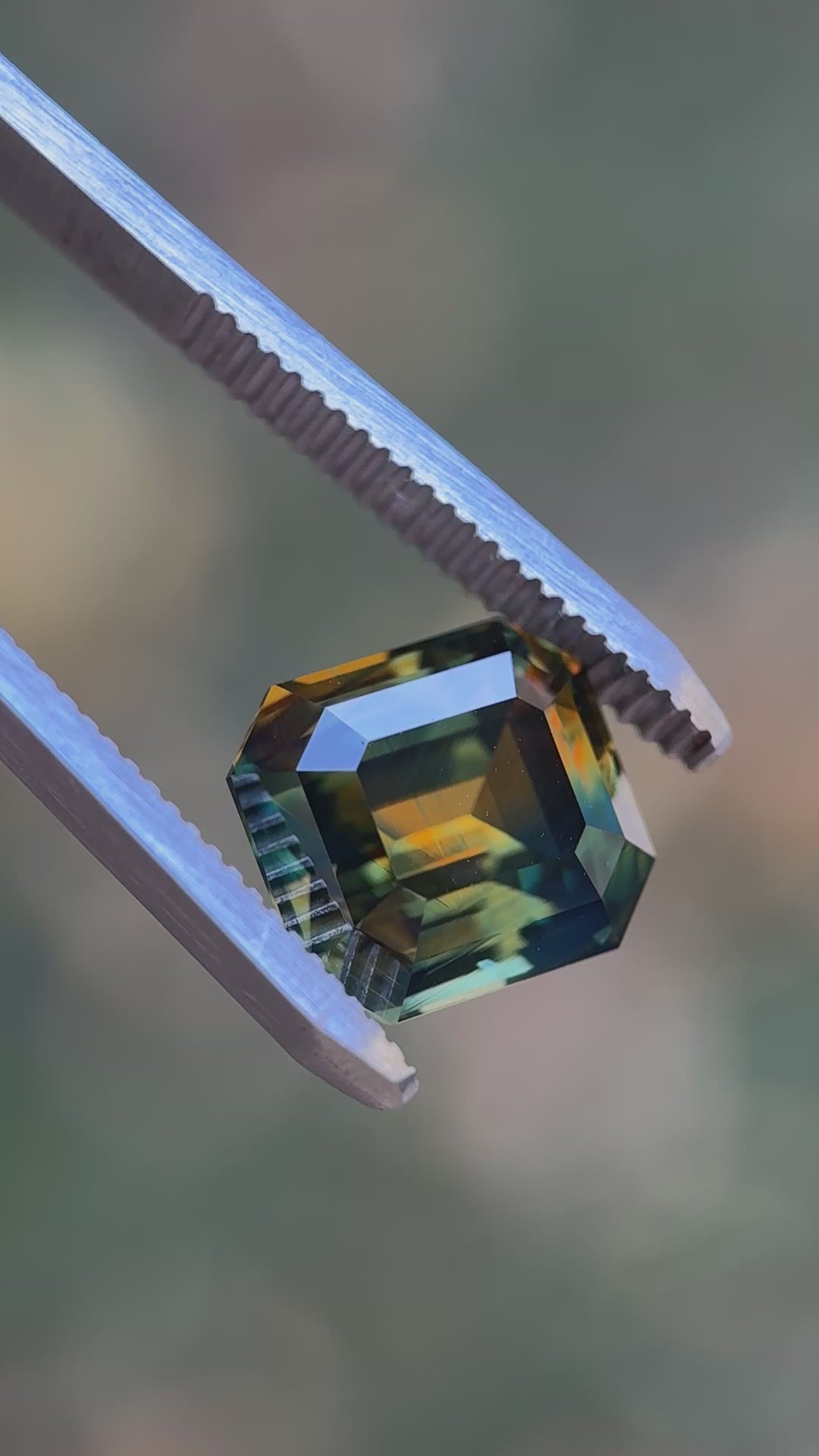 Macro video of a 9.14 carat Nigerian parti sapphire emerald cut, showing sharp facet reflections and distinct orange, yellow, blue, and green color zoning as the stone is viewed from multiple angles