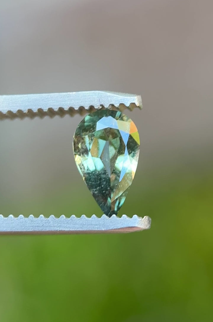 Rotating video of 1.06 carat sage teal green sapphire held in tweezers, showcasing sparkle and brilliance of pear cut gem from Umba River, Tanzania