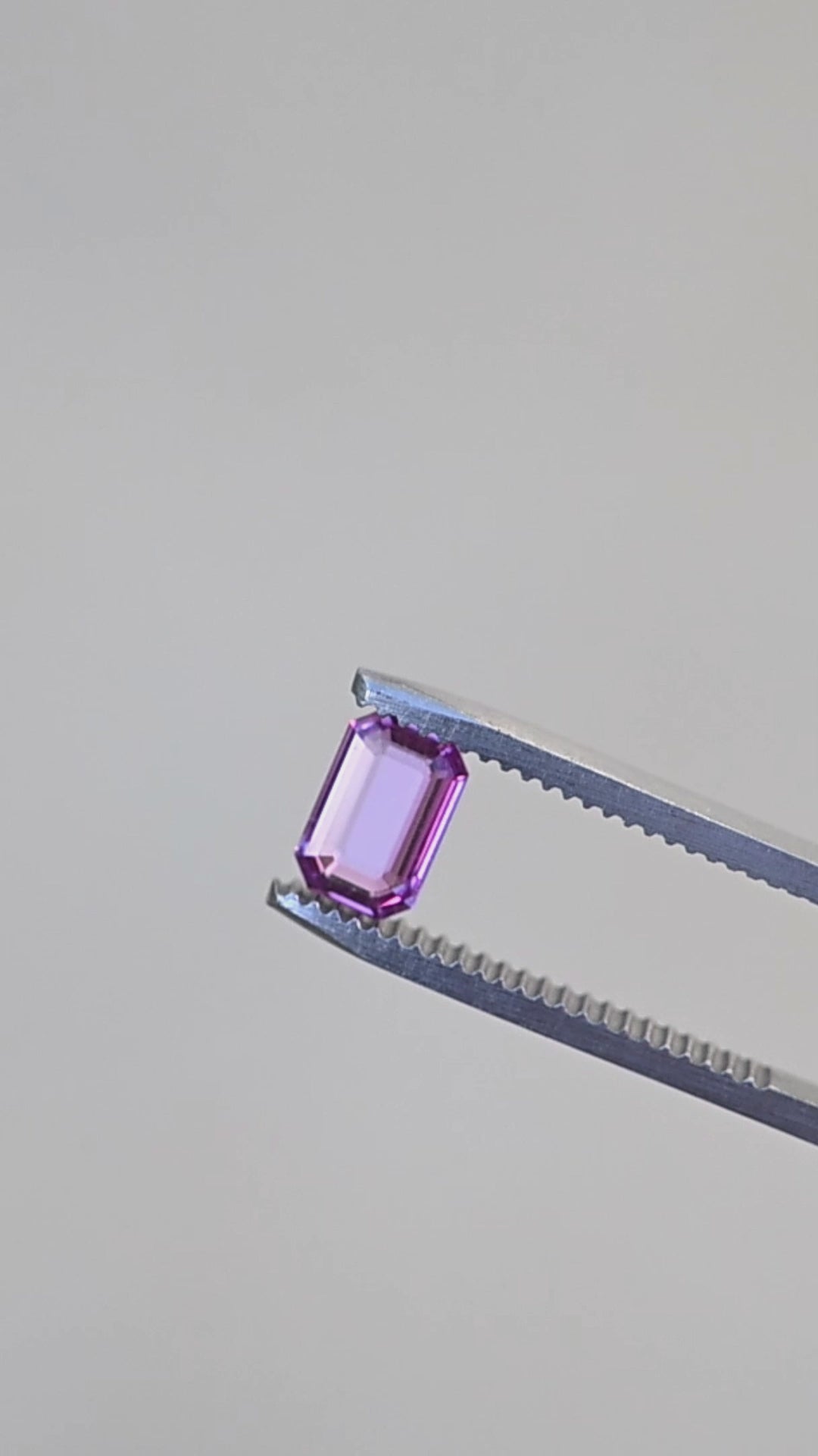Hot pink portrait cut sapphire rotating in gem tweezers under natural light.