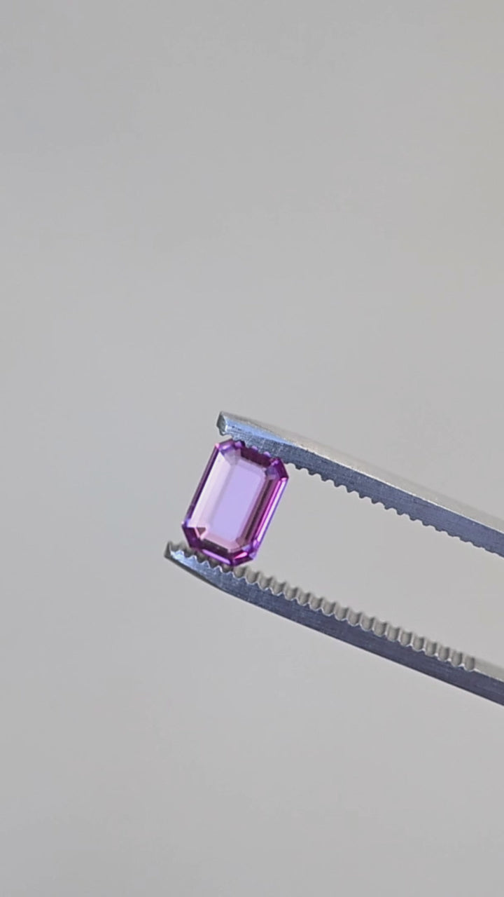 Hot pink portrait cut sapphire rotating in gem tweezers under natural light.