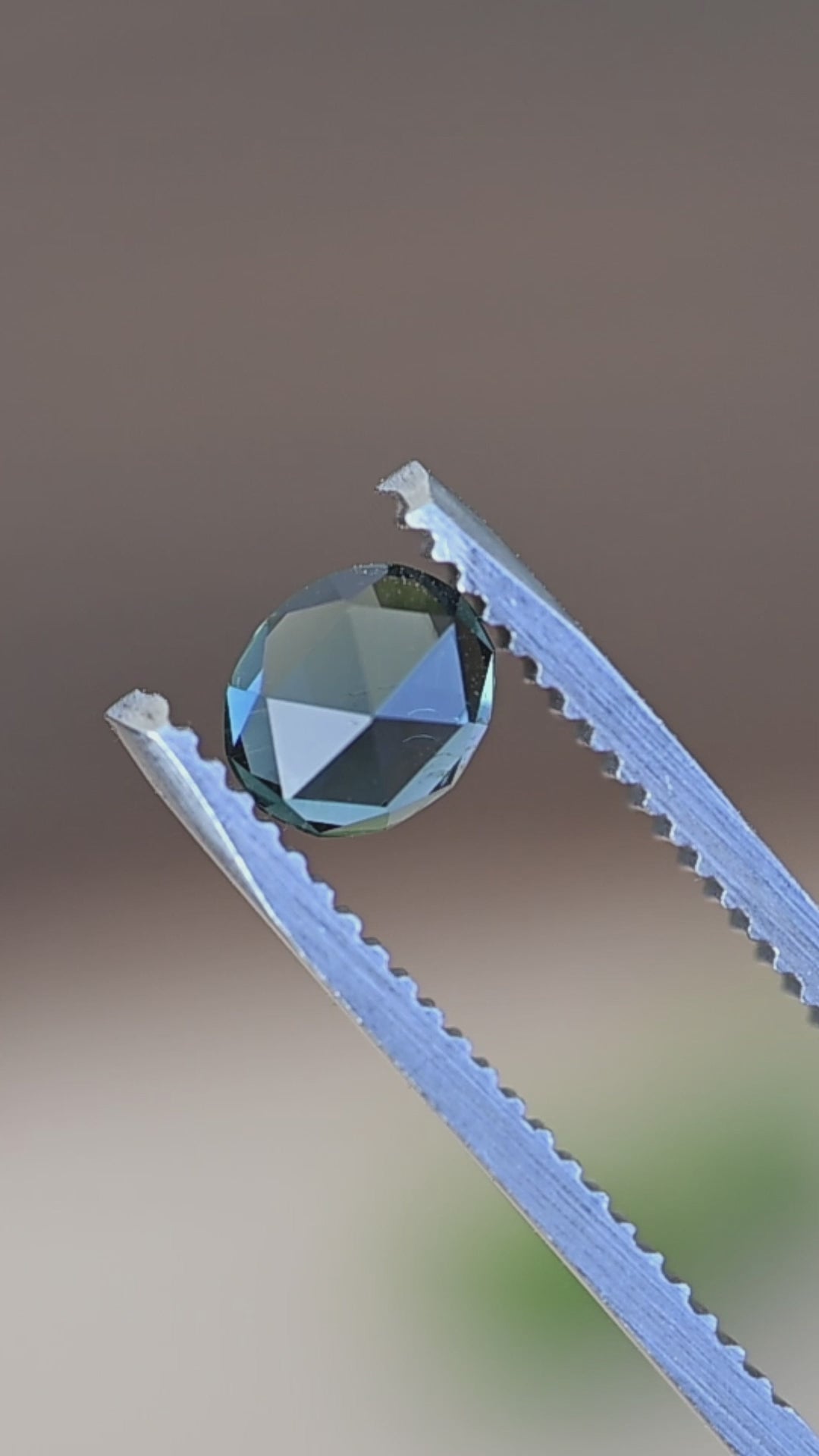 Oval teal Madagascar sapphire double rose cut held in tweezers rotating to show brilliance and color shift