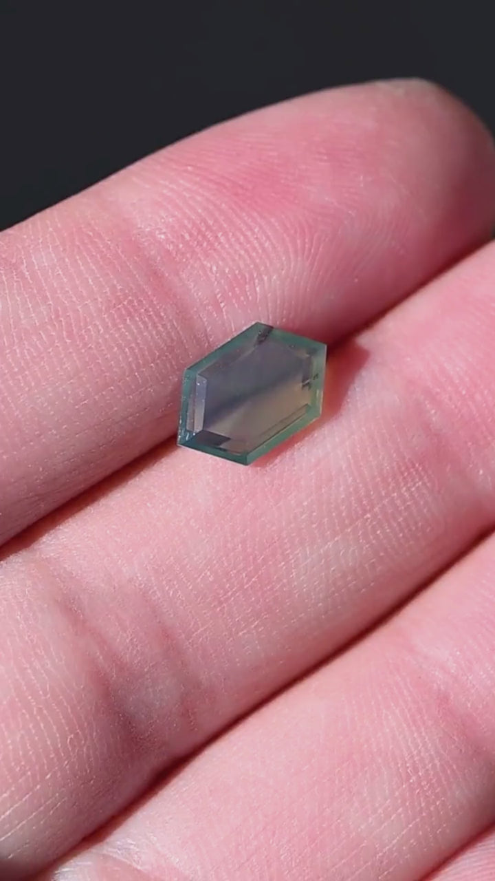 Explore a natural 2.15 carat opalescent teal green sapphire from Gombe, Nigeria, presented on the hand for scale. Completely untreated, this elongated hexagonal portrait-cut gemstone features a translucent blue-green appearance, fine internal texture and distinctive geometric proportions. An unusual loose sapphire for custom jewelry and contemporary designs.