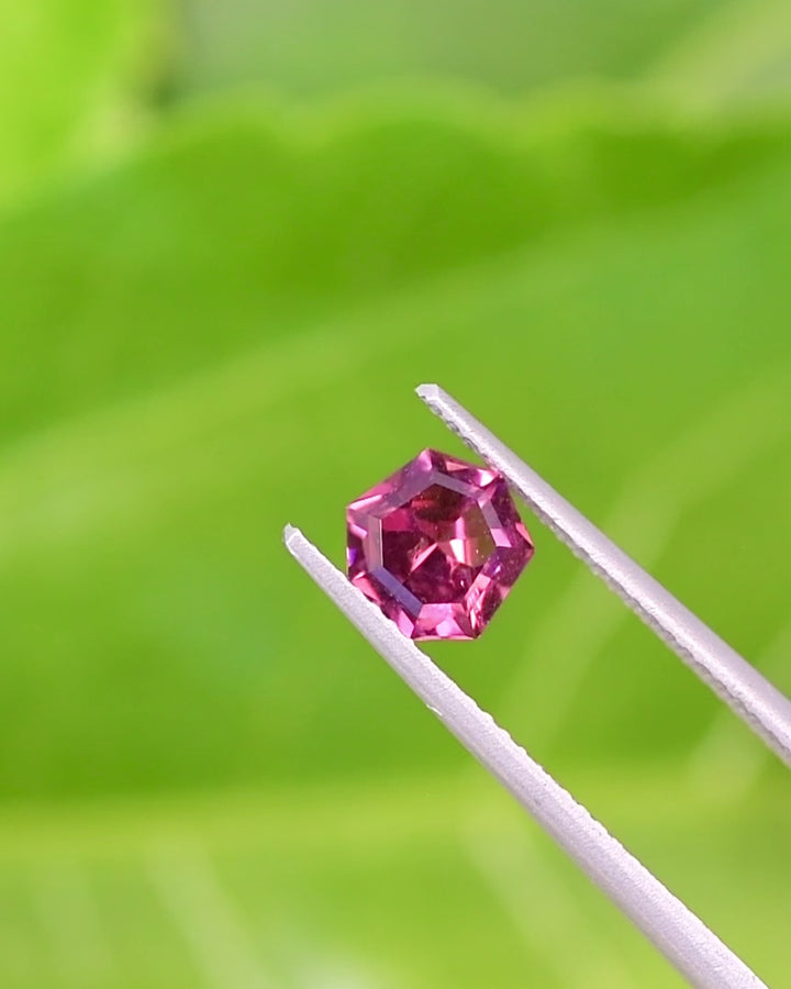 Video of 1.00CT red pink purple garnet rotating in tweezers under natural sunlight, highlighting its radiant color play and geometric shield cut symmetry, untreated gemstone from Kenya.