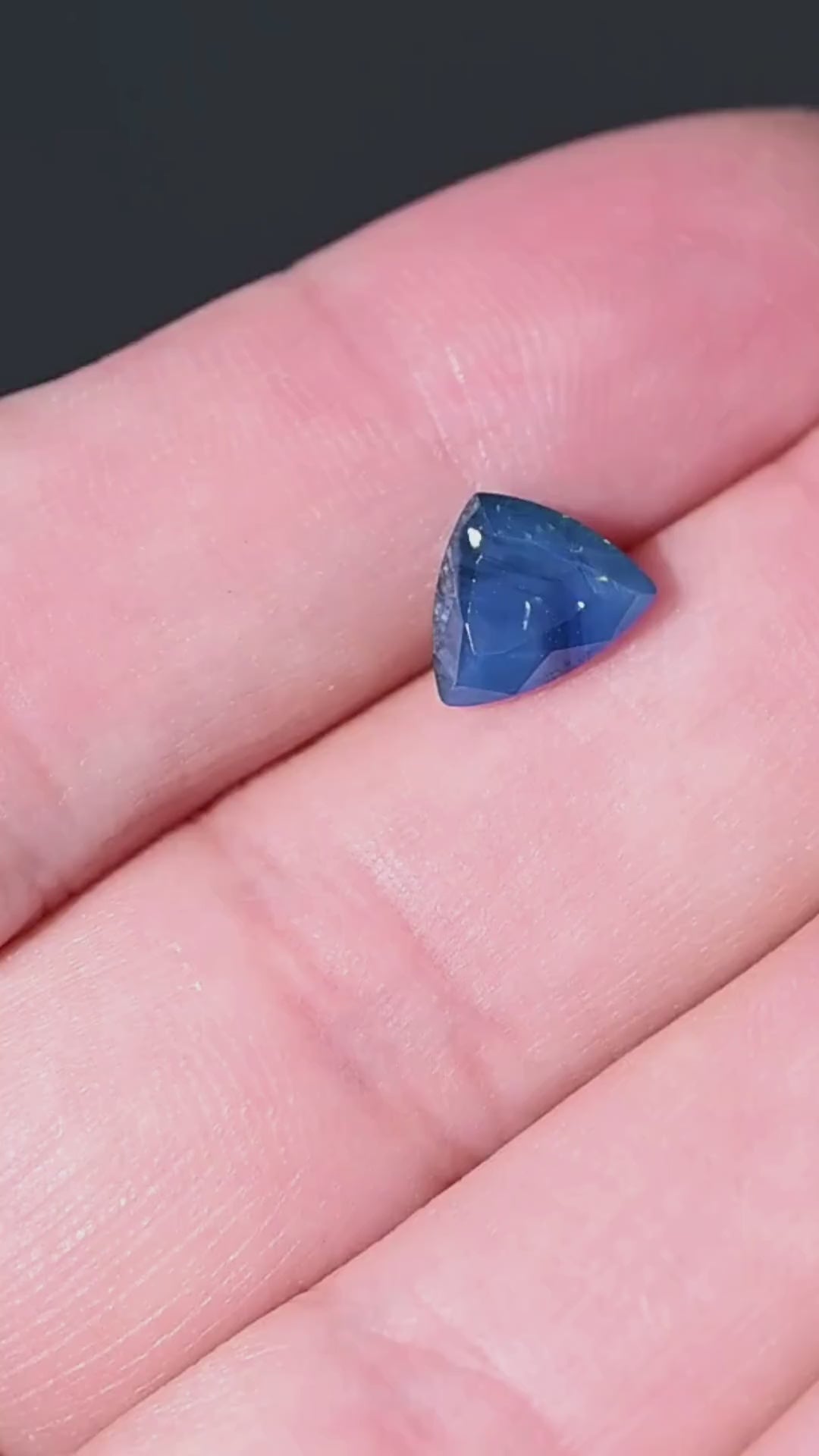 Discover a natural 1.91 carat opalescent royal blue sapphire from Gombe, Nigeria. This untreated gemstone features a custom trillion cut, distinctive internal texture and rich blue coloration. Shown against the hand for scale, it offers an unusual choice for bespoke engagement rings and custom jewelry.