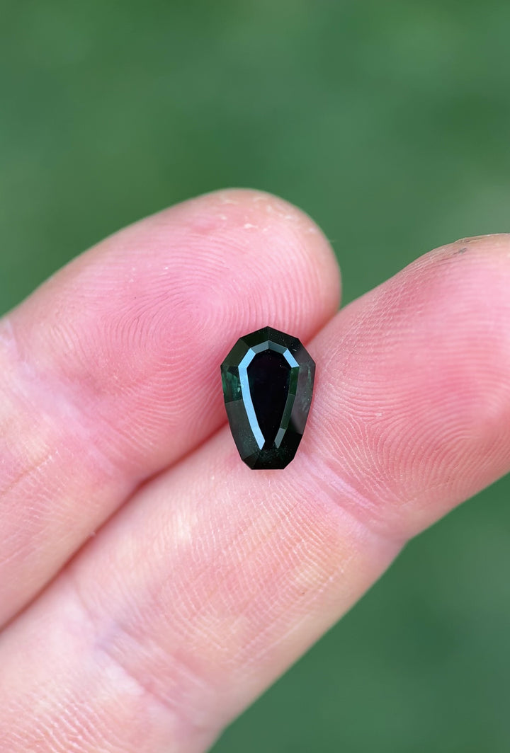 Rotating 3.07ct shield cut sapphire from Nigeria, capturing the gem's step-cut facets and moody blue-green color play in daylight.