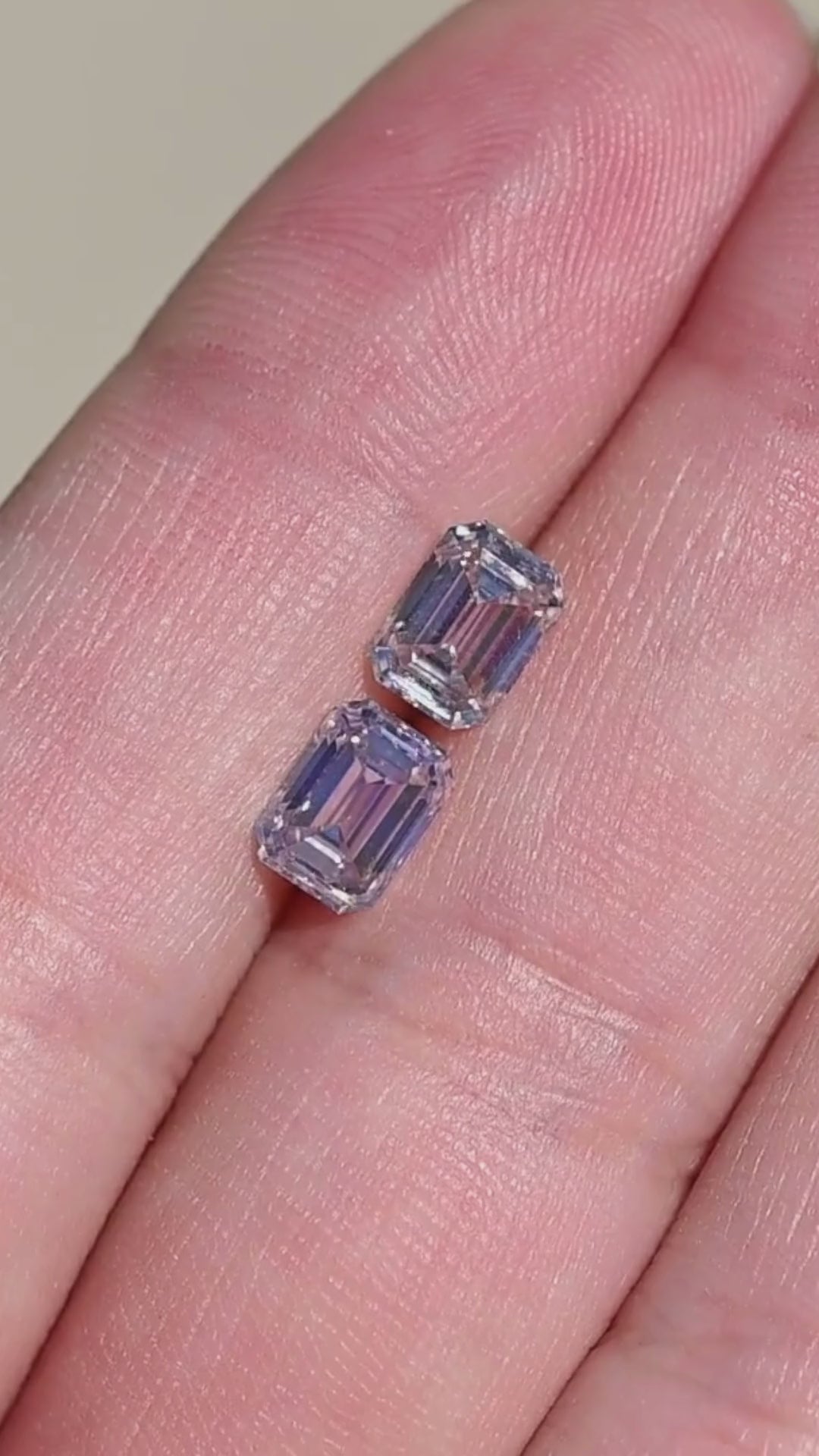 Two natural light rosy brown emerald cut Canadian diamonds shown in direct sunlight, highlighting brighter champagne and blush flashes, VVS clarity and the mirrored movement of their step-cut facets.