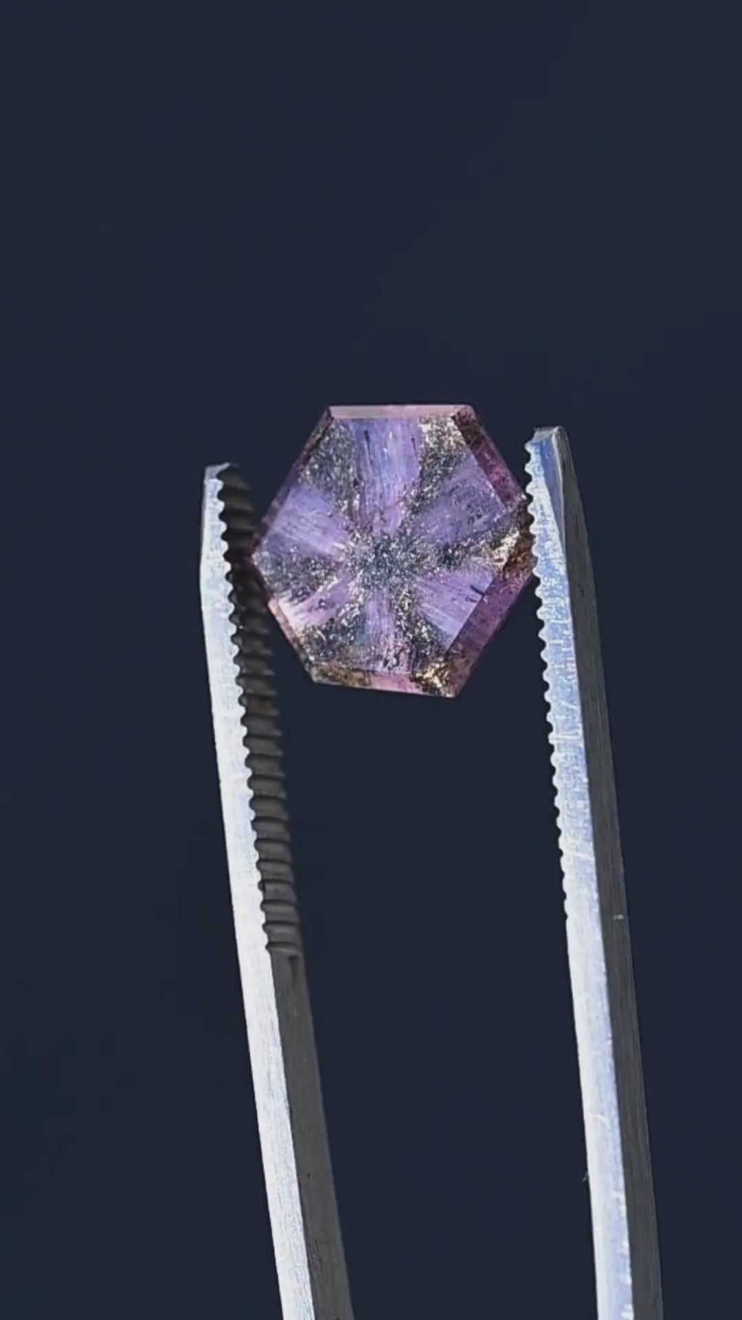 Discover the internal architecture of a 5.56ct untreated Afghan sapphire through close-up tweezer footage. The hexagonal portrait cut reveals a remarkable six-rayed pattern of dark inclusions against translucent lavender and orchid-pink crystal. Its distinctive natural markings make this sapphire an exceptional choice for collectors and custom jewelry designers.