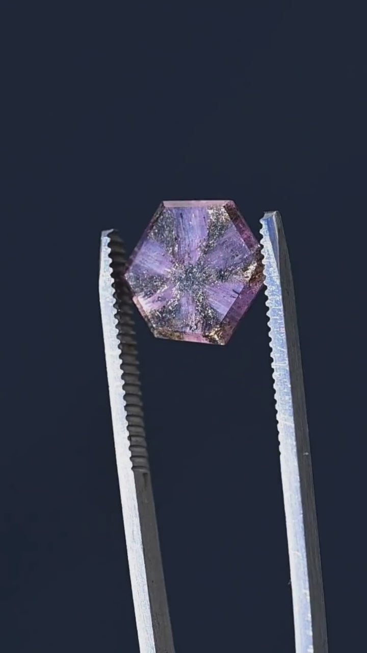 Discover the internal architecture of a 5.56ct untreated Afghan sapphire through close-up tweezer footage. The hexagonal portrait cut reveals a remarkable six-rayed pattern of dark inclusions against translucent lavender and orchid-pink crystal. Its distinctive natural markings make this sapphire an exceptional choice for collectors and custom jewelry designers.