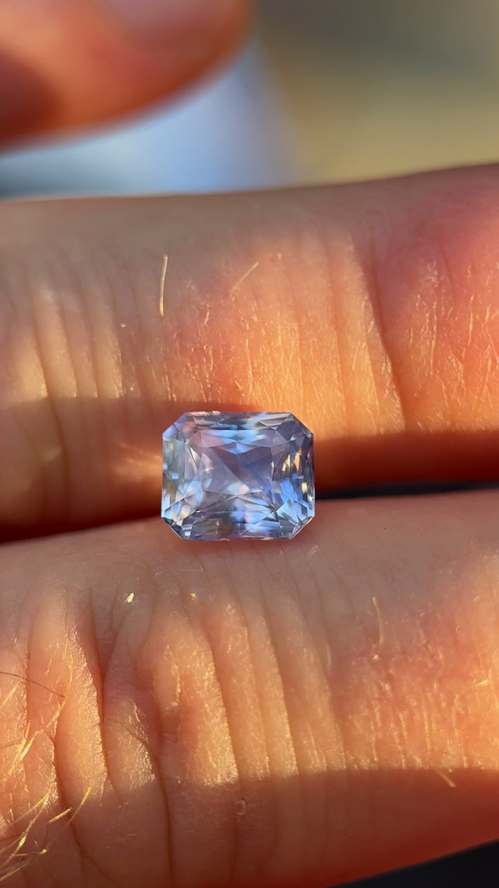 Handheld video of a 2.70ct radiant cut sapphire with lavender, blue, and violet hues, showcasing the gemstone’s fire and clarity in motion.